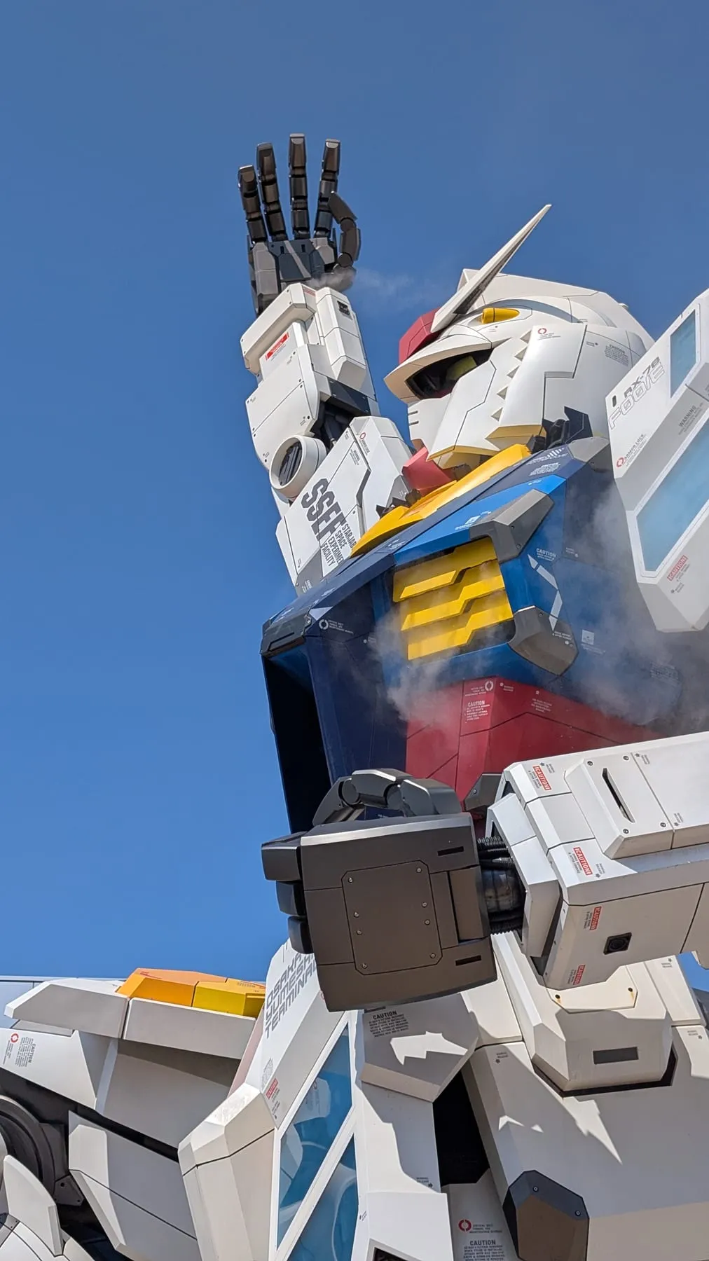 Il Gundam a grandezza naturale visto dal basso contro il cielo azzurro