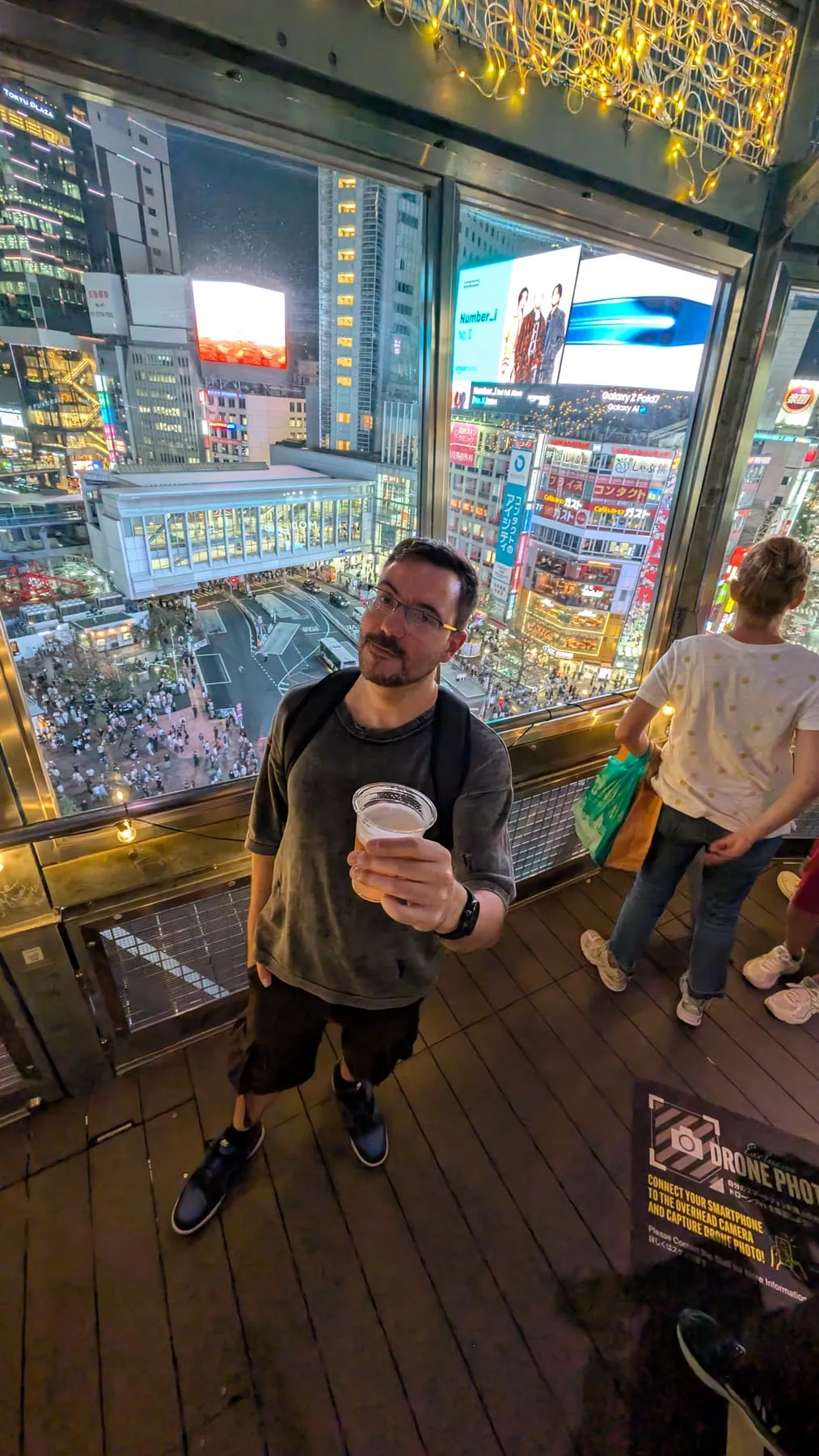 Robugin con una birra su una terrazza affacciata sull'incrocio di Shibuya illuminato di sera