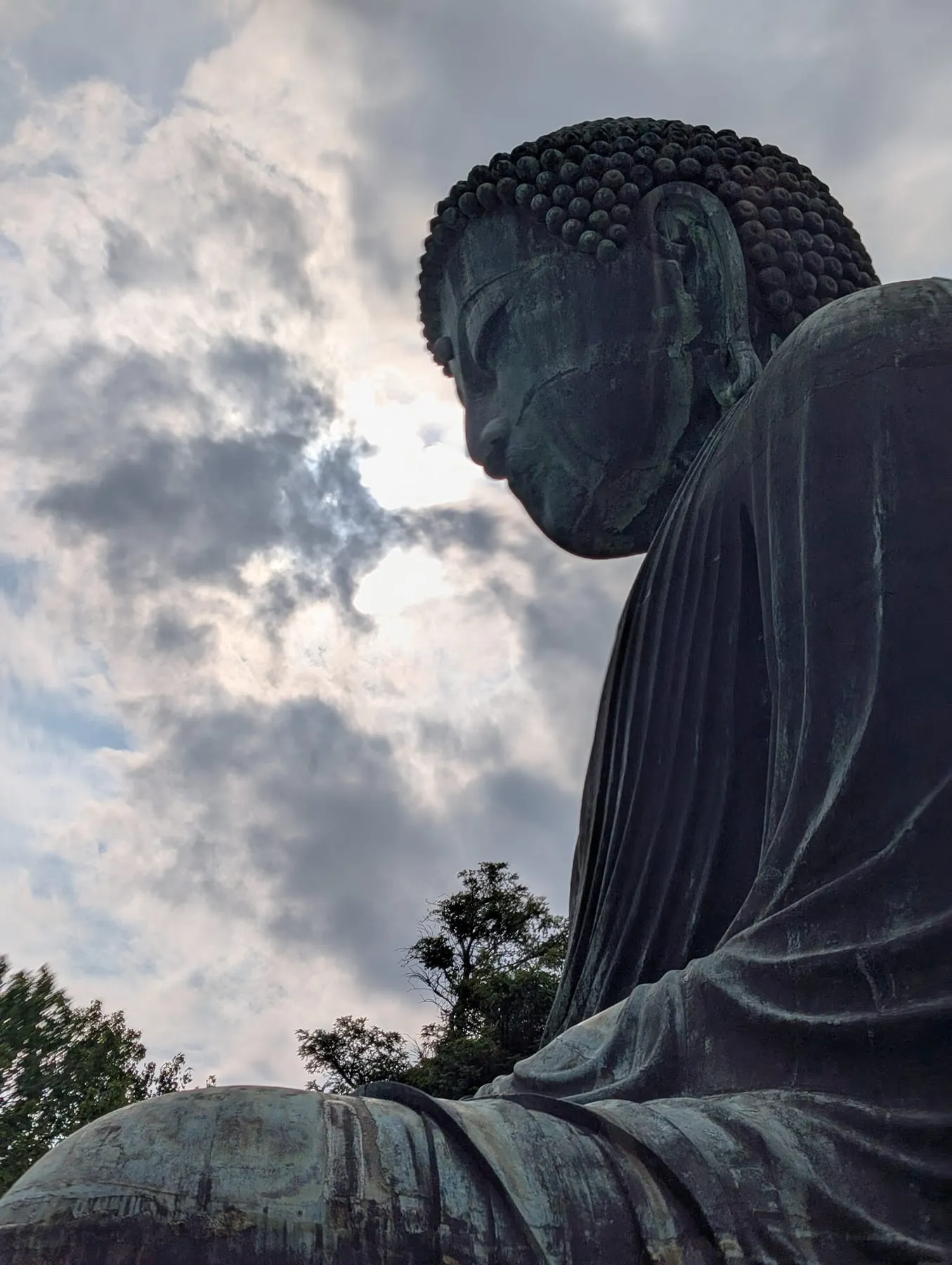 Il Grande Buddha di bronzo di Kamakura visto di profilo contro un cielo nuvoloso